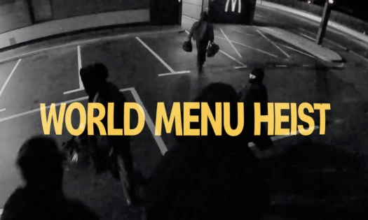 The text in bold, "WORLD MENU HEIST" superimposed on CCTV footage of thieves raiding a McDonald's