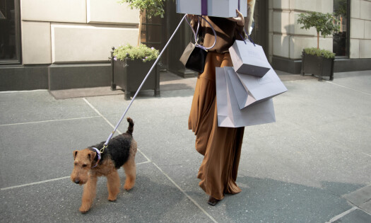 A woman carrying gift boxes and shopping bags coming out of the department store with her dog