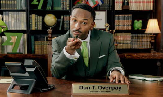 Mohammed Mohammed playing "Don. T Overpay," dressed in a suit and sitting at a desk in front of a bookcase