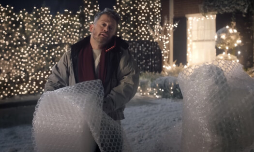 Actor Macaulay Culkin standing in front of a home decorated with white Christmas lights