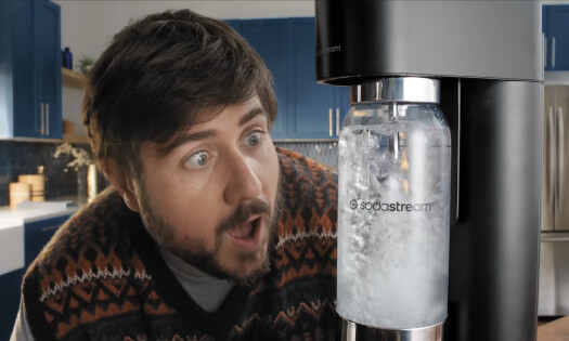 A man is seen beside a SodaStream machine, excitedly watching as it carbonates water