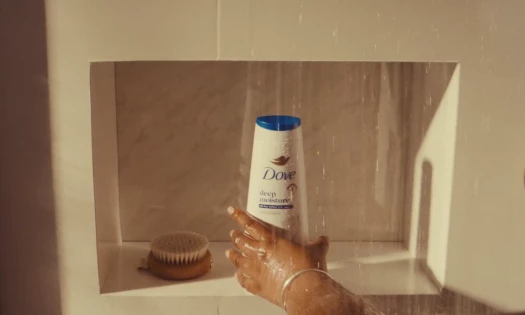 A person grabbing a Dove shower cream in the shower