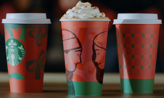 Three Starbucks cups sitting on a table, showing this year's holiday-themed illustrations