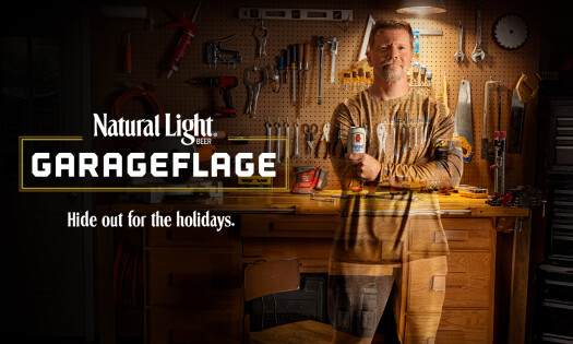 A man standing in a garage holding a Natural Light beer wearing the Tinkerer's outfit in the Garageflage collection