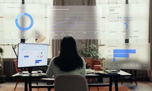 The back of a woman in front of a computer with pop-up screens of different analytics in Google Ads' 25-year anniversary video