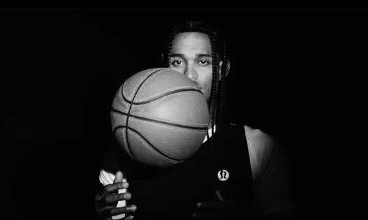 NBA player Jordan Clarkson is shown ready to catch an airborne basketball, in a black and white screenshot with a black backdrop