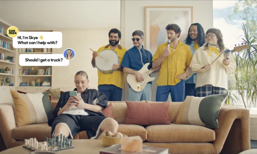WNBA player Paige Brueckers seated at a couch inside a sunny living room using her phone, with a band behind her