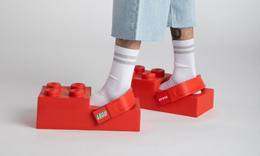 The LEGO Brick Clog shown on a model, which are oversized shoes resembling red LEGO bricks