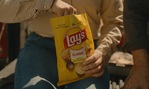 A person holding a bag of Lay's potato chips, which shows its refreshed branding with sun rays coming out of the logo