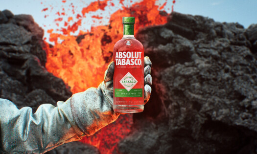 A hand holding a bottle of the Tabasco-infused Absolut vodka against a volcanic backdrop