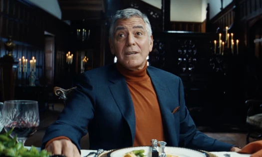 Actor George Clooney pictured in an expensive suit, sitting inside a stately mansion