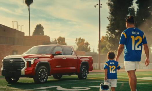 A man and a little boy wearing football jerseys are shown holding hands in front of a red Toyota RAV4