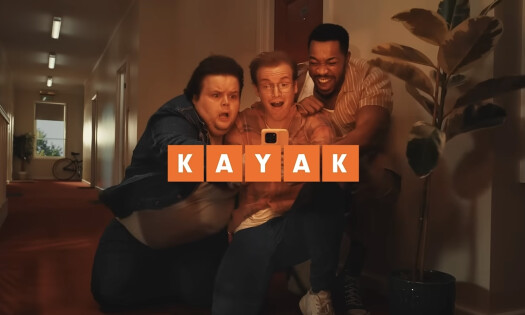 Three guys huddled around a phone looking scared, with the KAYAK logo shown overtop of the shot