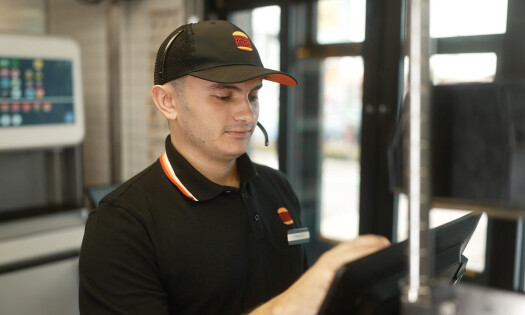 A drive thru employee at Burger King wearing a headset talking to AI assistant "Patty"