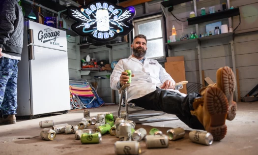 Jason Kelce pictured in front of a "Garage Beer" labeled fridge, with beer cans around him on the floor