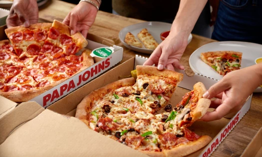 A photo of hands pulling slices from Papa John's pizzas on a table