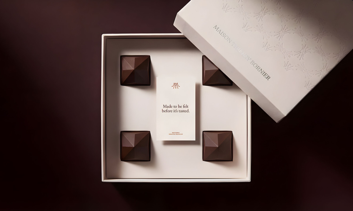 Open luxury chocolate box with four geometric chocolates arranged in compartments and a central