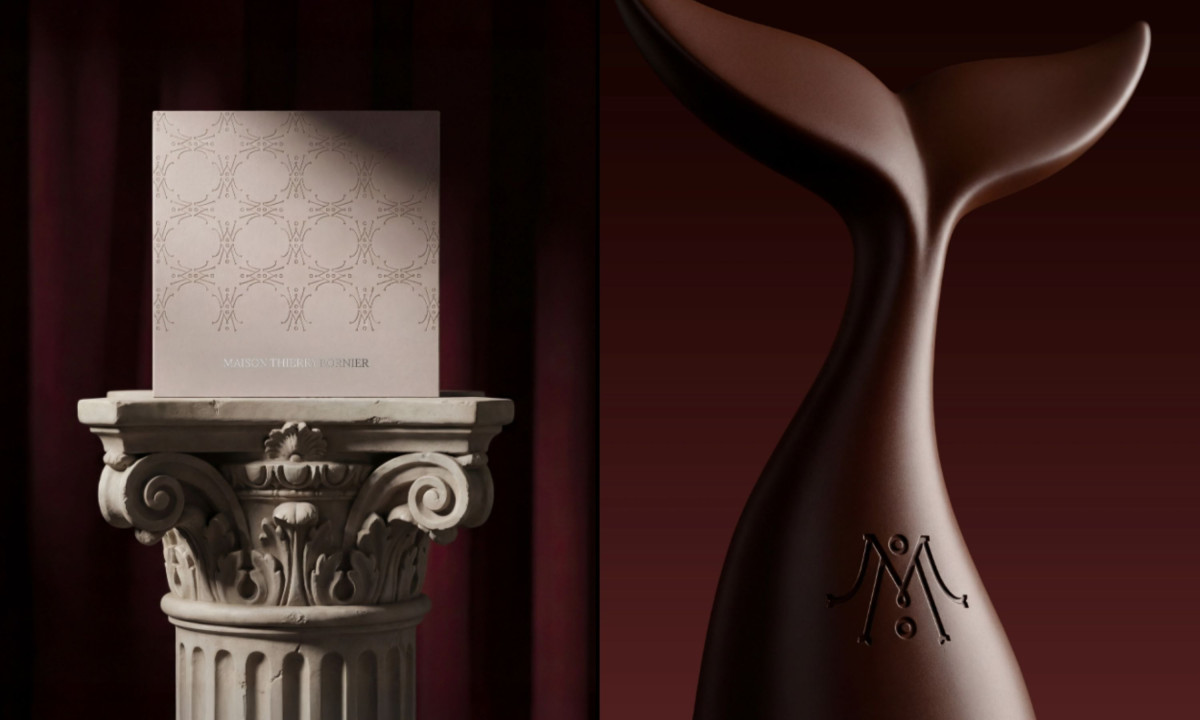Branded box with repeating monogram pattern displayed on a classical pedestal next to sculptural object