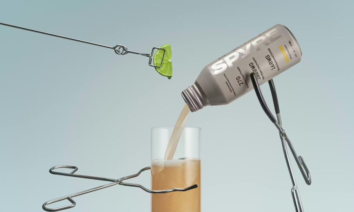 Liquid pouring from a SPYRE bottle into a glass held by metal tongs