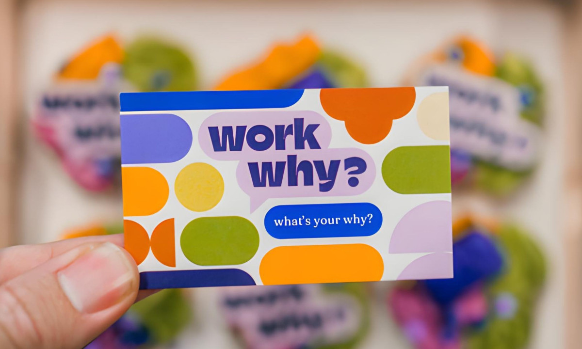 A person holding a colorful "Work Why?" business card
