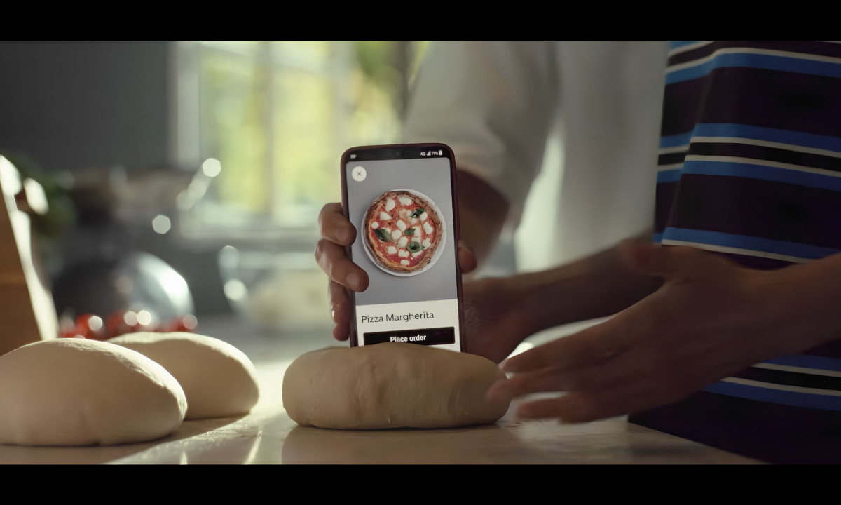 Person plants a smartphone displaying pizza into dough.