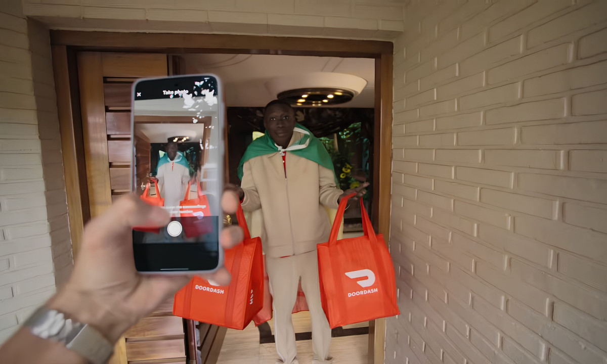 A smartphone photographs a man holding red delivery bags.