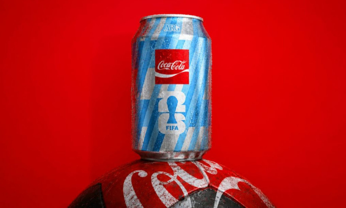 A striped Coca-Cola can sits atop a soccer ball.