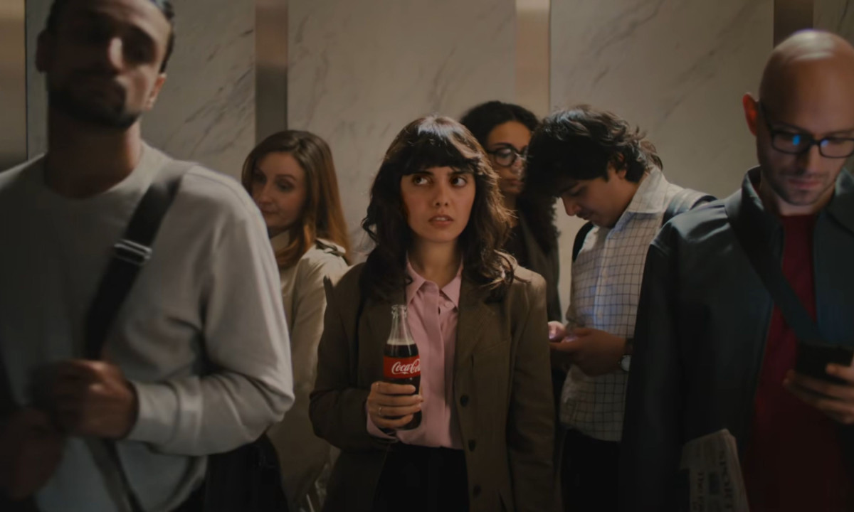 A woman holds a Coca-Cola bottle inside a crowded elevator.