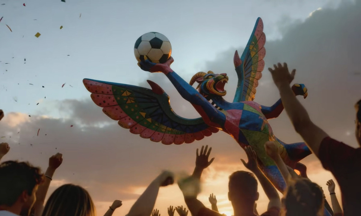 Cheering crowd reaches toward a colorful winged creature sculpture.