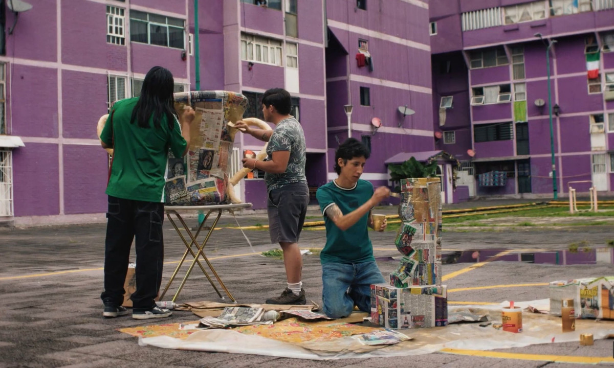 Three young men construct a large papier-mâché trophy in a residential courtyard.