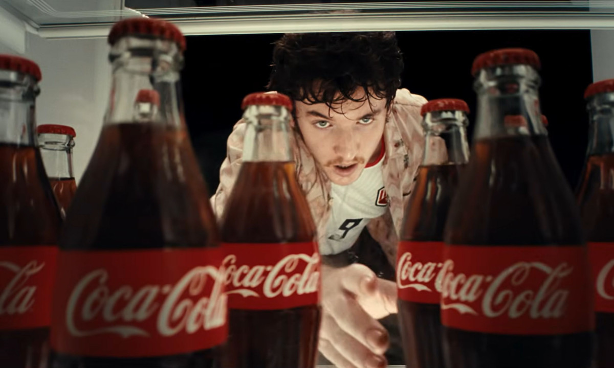 A young man reaches into a refrigerator filled with Coca-Cola.