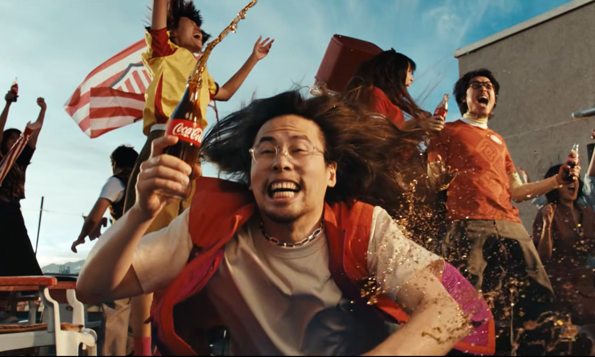 Ecstatic fans celebrate on a rooftop while Coca-Cola splashes around.