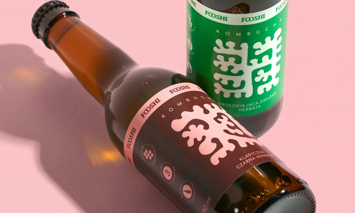 Two Fooshi kombucha bottles resting on a light pink surface.