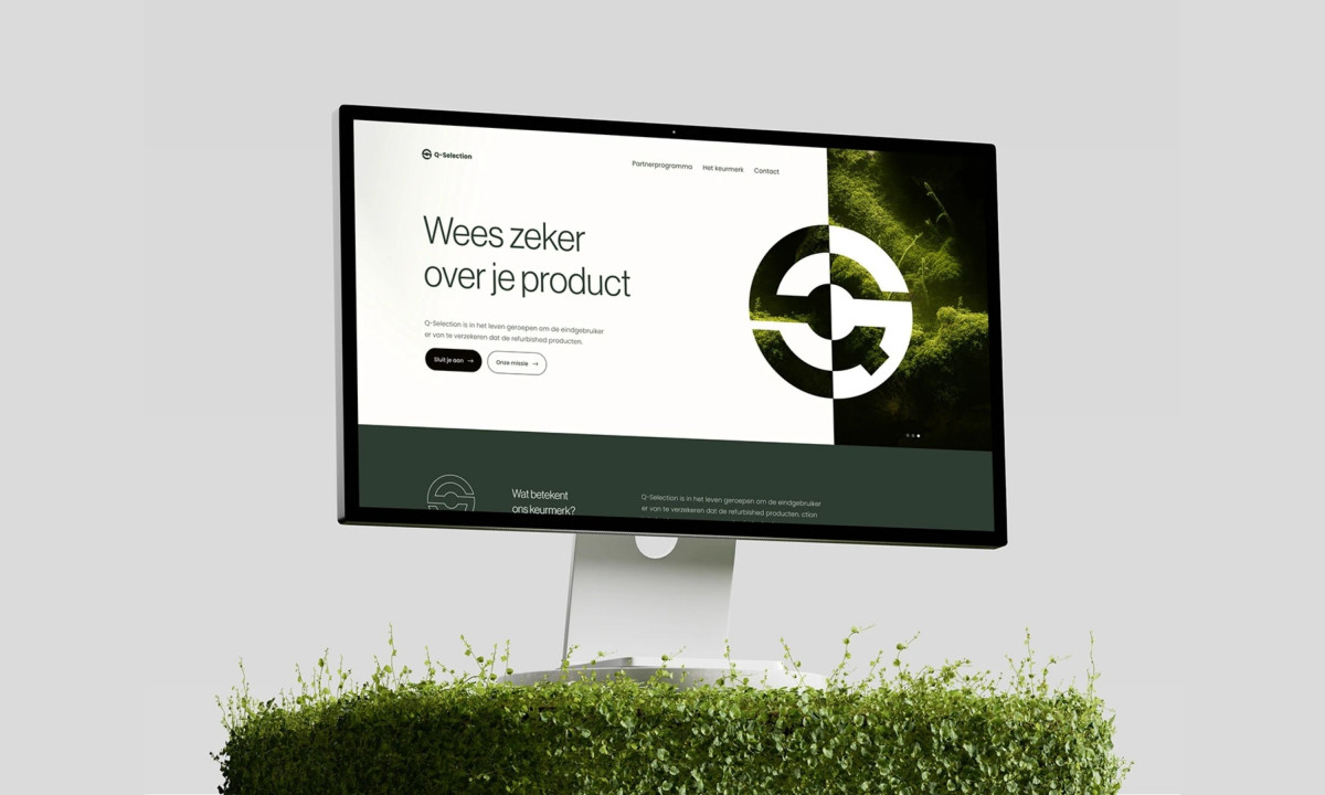 Computer monitor displaying a website with a large logo, resting on green plants.
