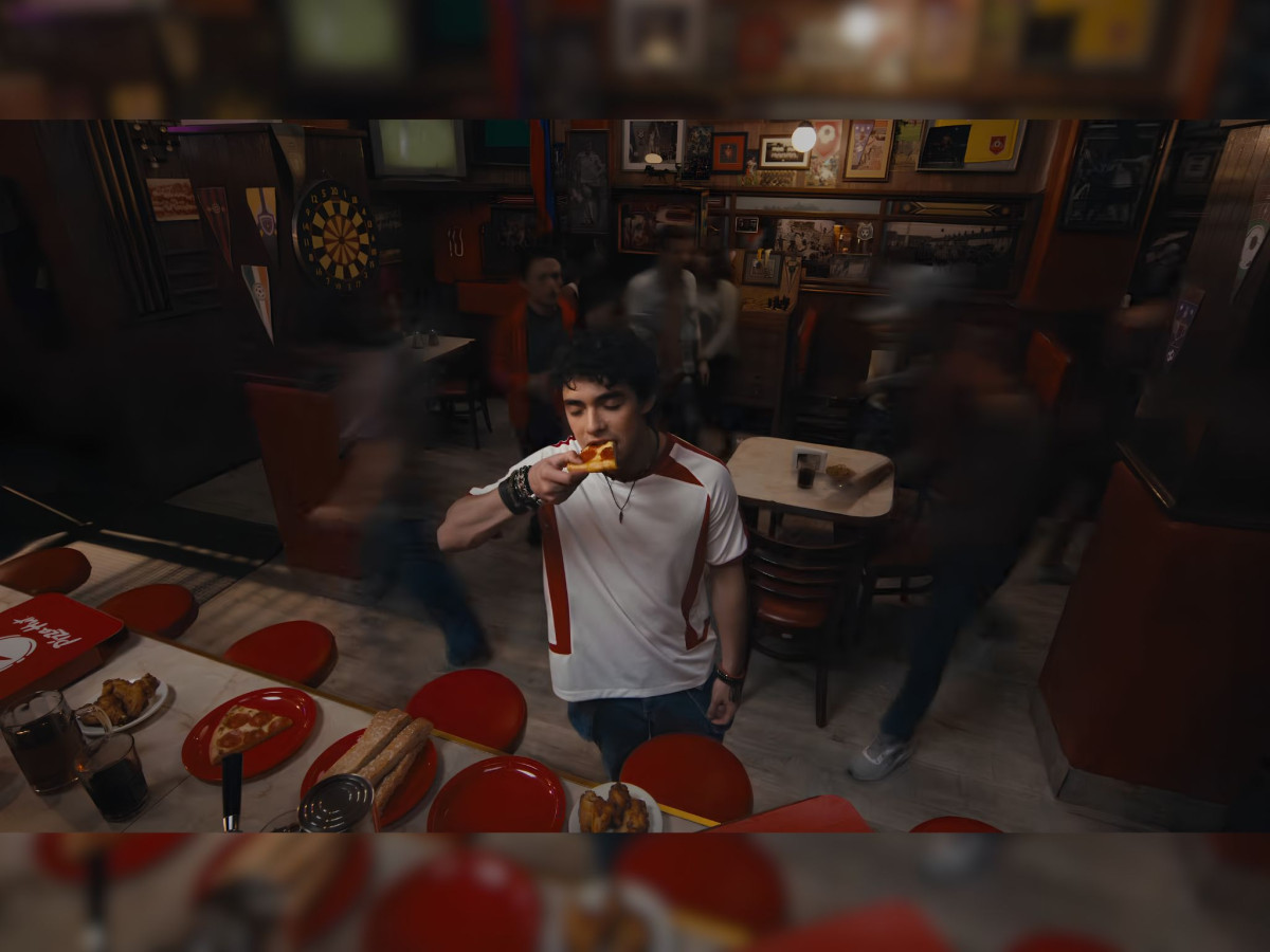 A young man eats pizza in a blurred, nostalgic pub.