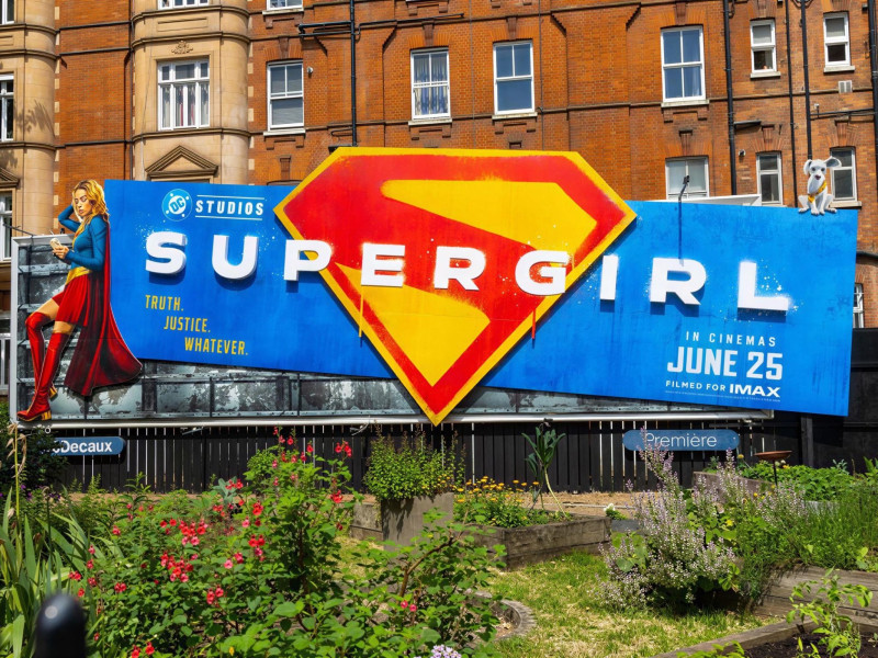 Supergirl and dog on a billboard in a garden.