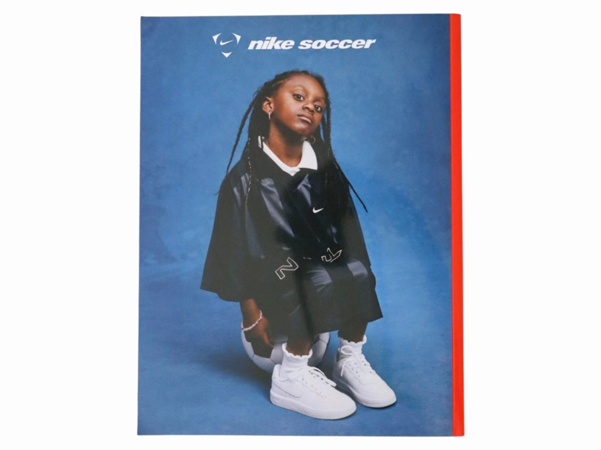 Nike soccer magazine cover featuring a young girl in athletic wear sitting on a soccer ball against a blue background.