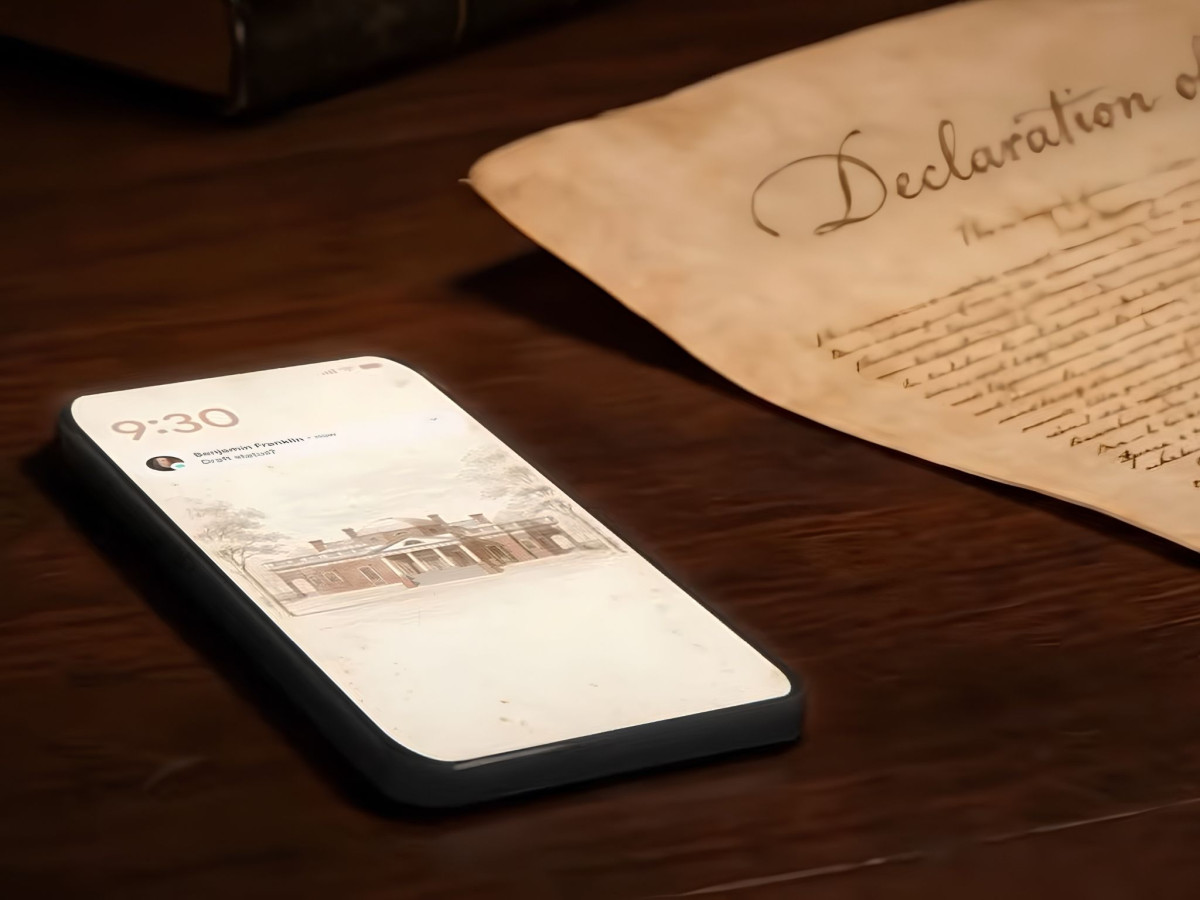 A smartphone resting next to a parchment Declaration of Independence on a wooden desk.