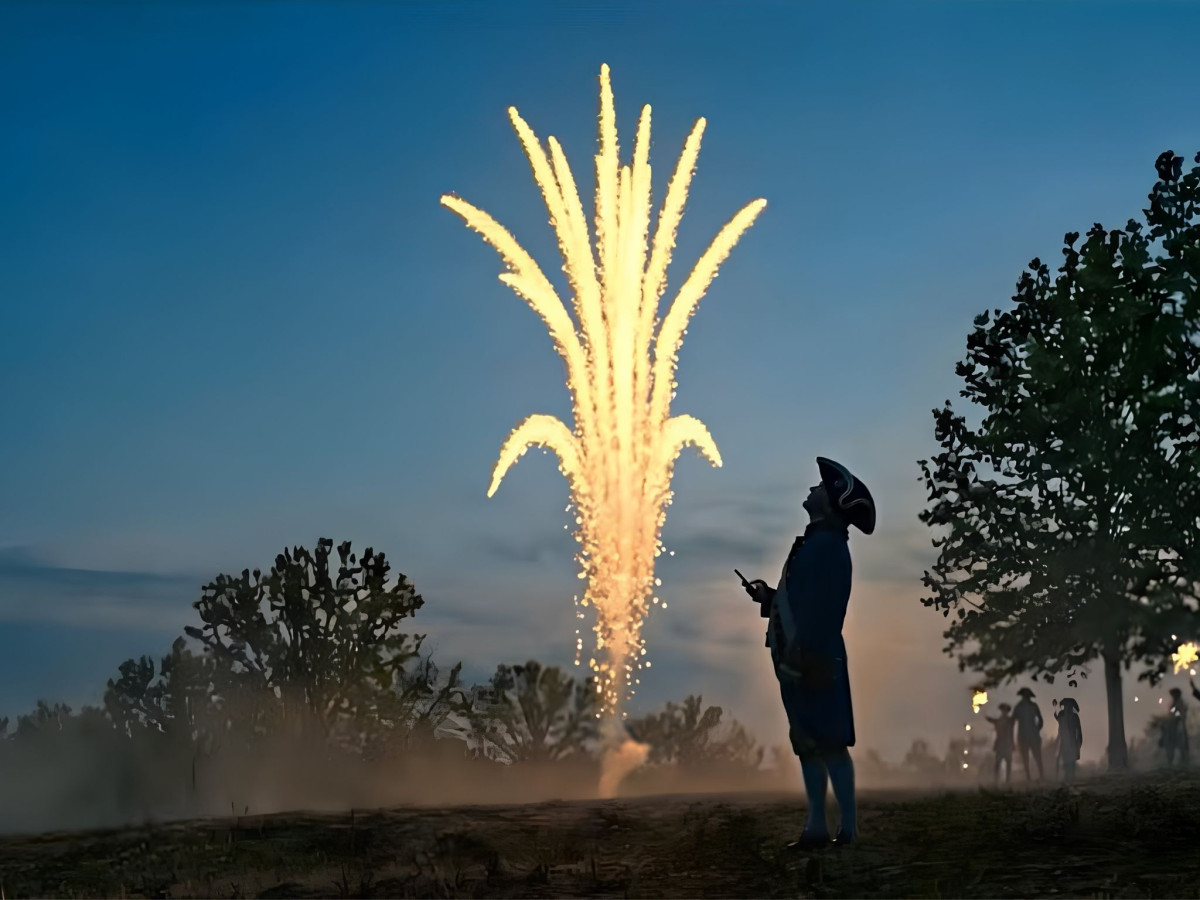 Silhouette of a man in colonial attire standing in a field watching a large golden firework.