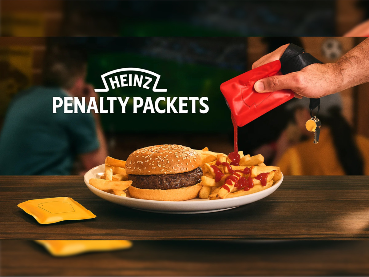 Hand squeezing red Penalty Packet ketchup onto fries.