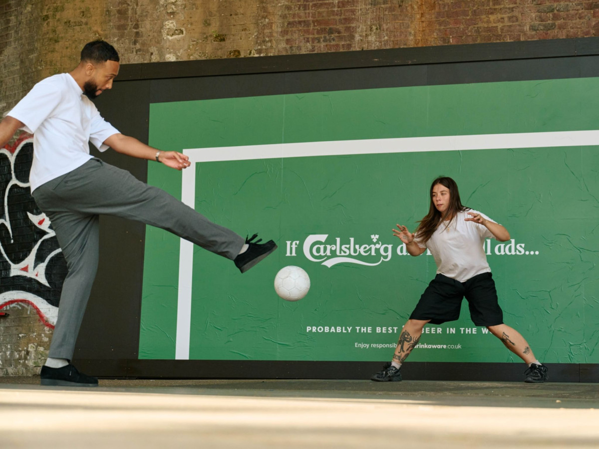 Two people playing football near a Carlsberg goal billboard.