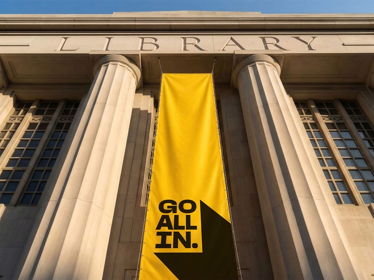 Yellow GO ALL IN banner hanging outside a library building.