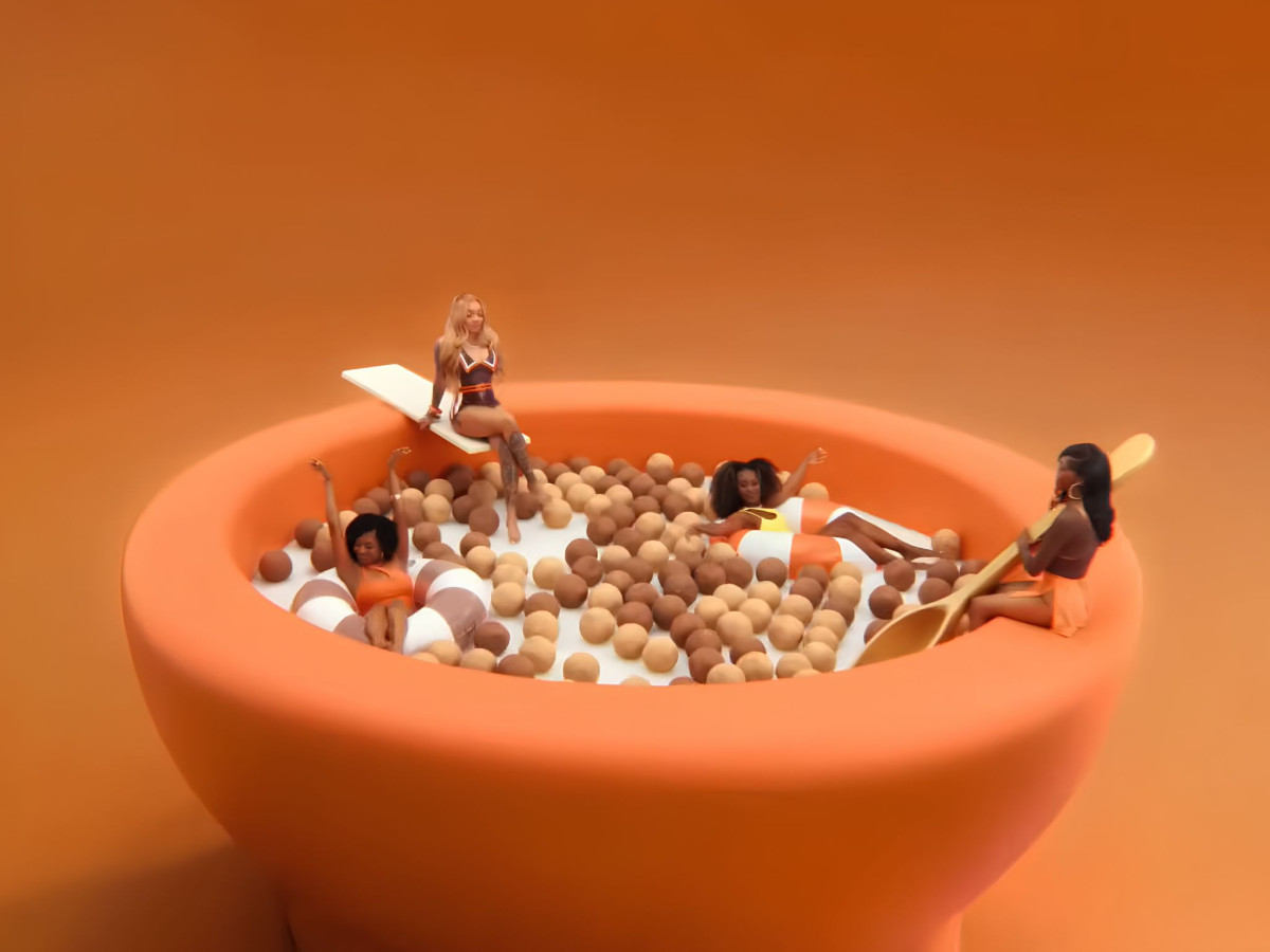 Women lounging in inner tubes and on a diving board inside a giant bowl of Reese's Puffs cereal.