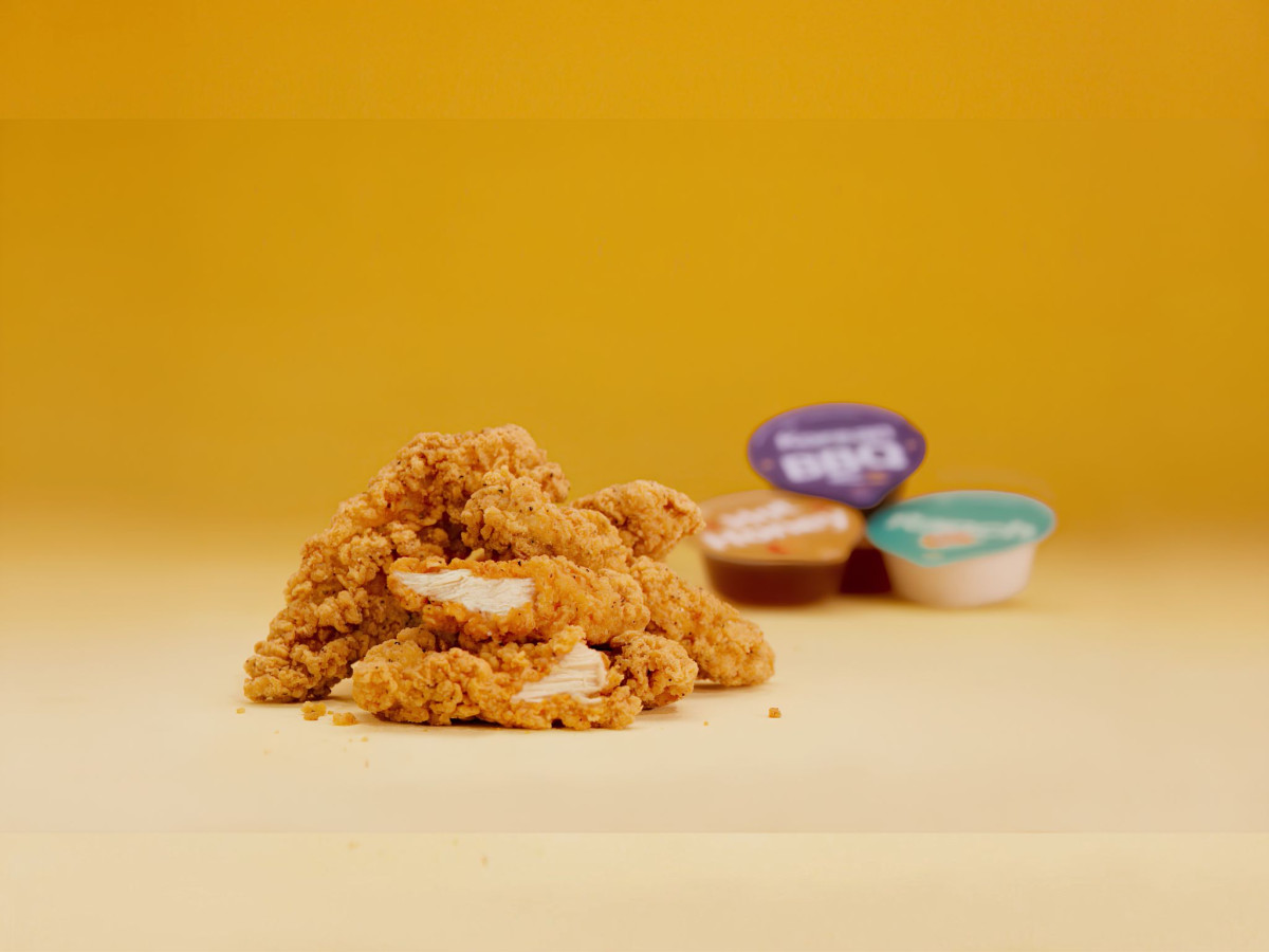 Focused crispy chicken strips with blurred sauce tubs on a yellow background.