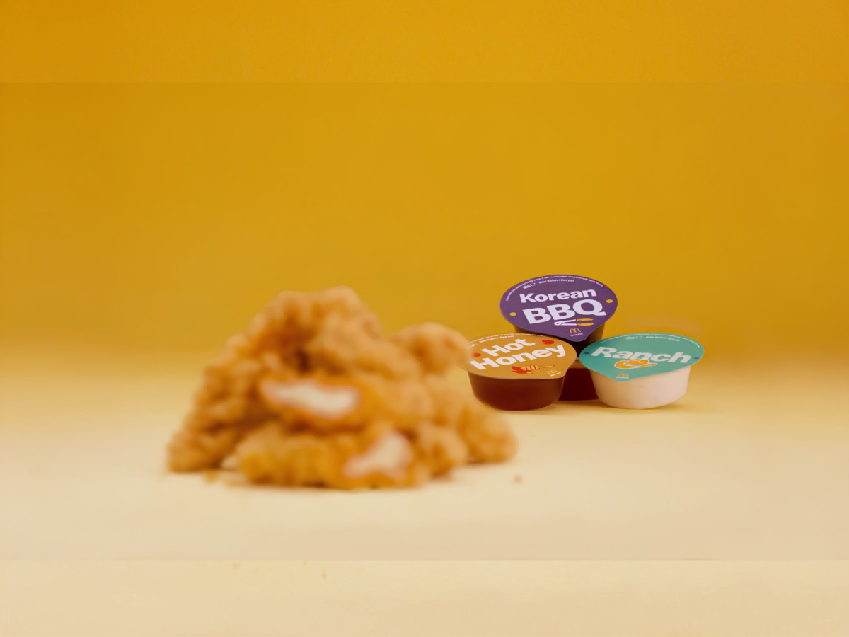 Focused McDonald's sauce tubs with blurred chicken strips on a yellow background.
