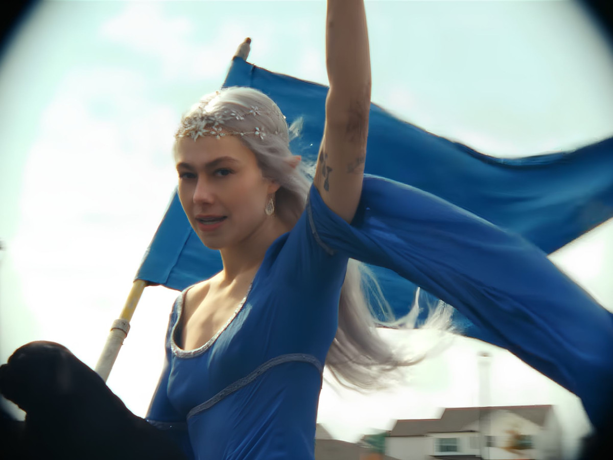 Phoebe Bridgers in a blue medieval-style dress holding a blue flag.