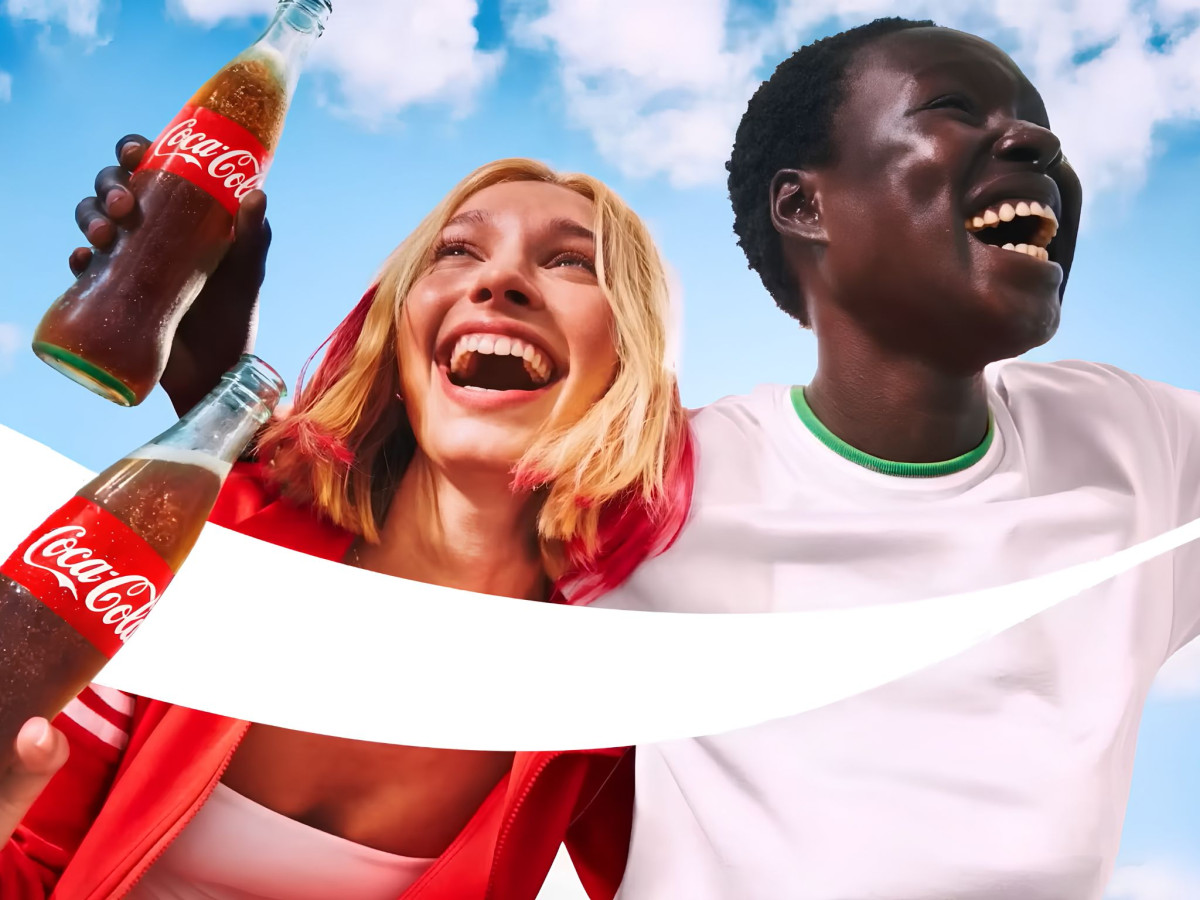 Two smiling people holding Coca-Cola bottles against a blue sky.