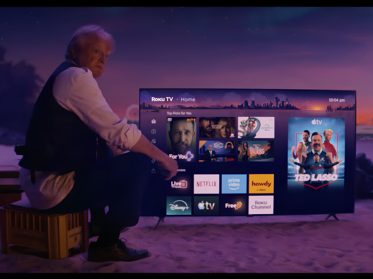 Man sitting on a beach beside a TV displaying the Roku interface.