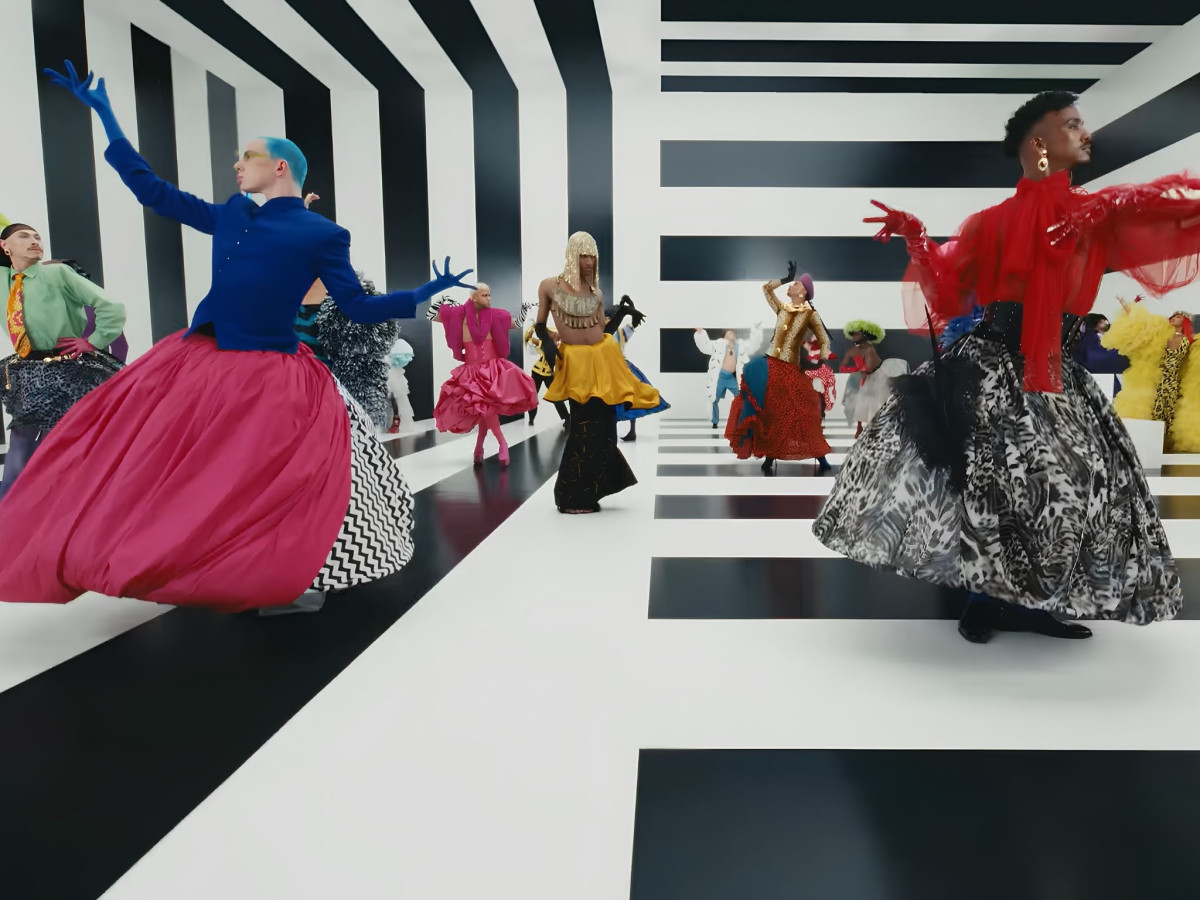 Dancers wearing vibrant, high-fashion garments performing dynamic choreography inside a bold black-and-white striped room.