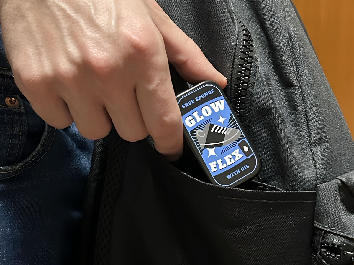 Person placing a compact Glow Flex tin into a black backpack pocket.